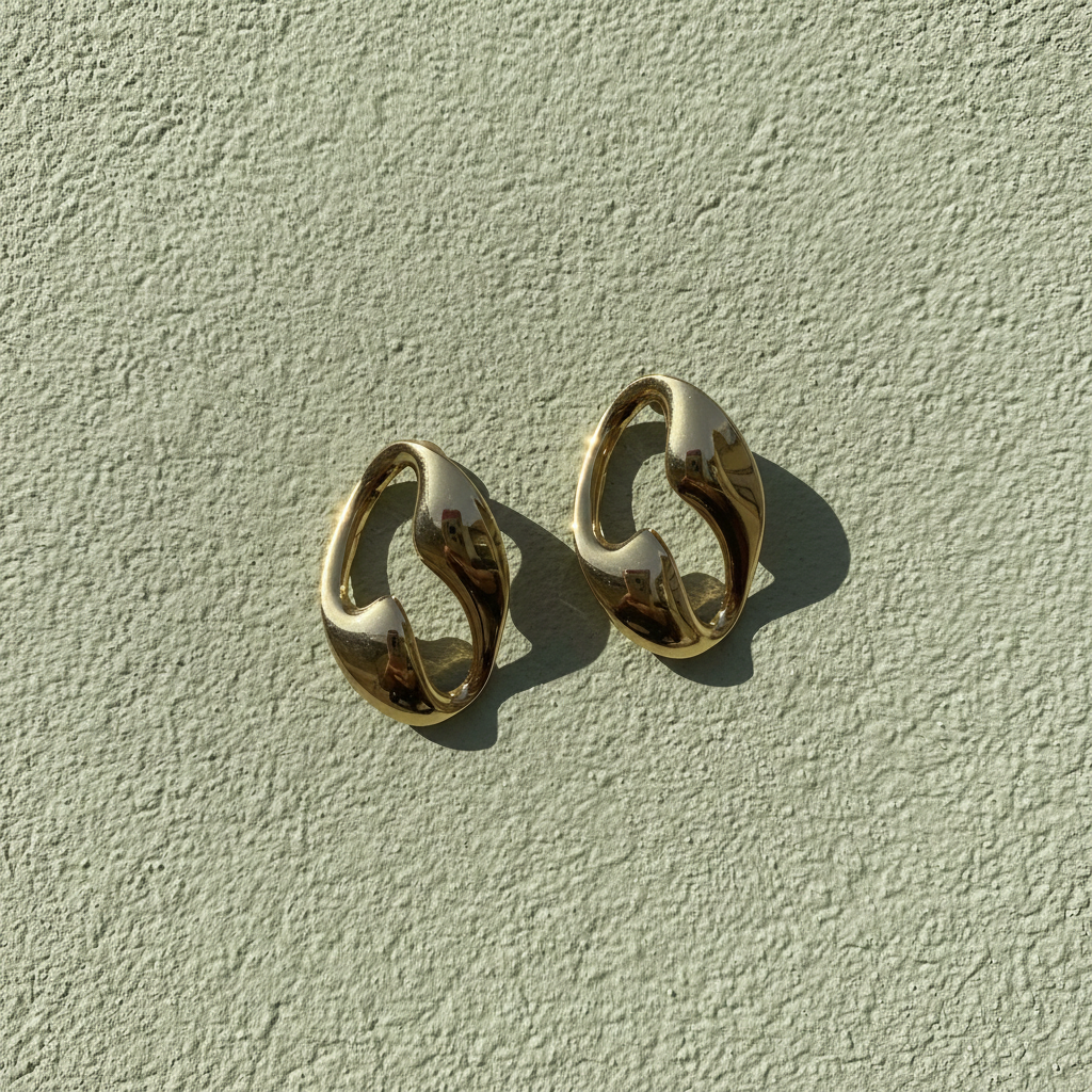 Gold oval hoop earrings on sage green plaster