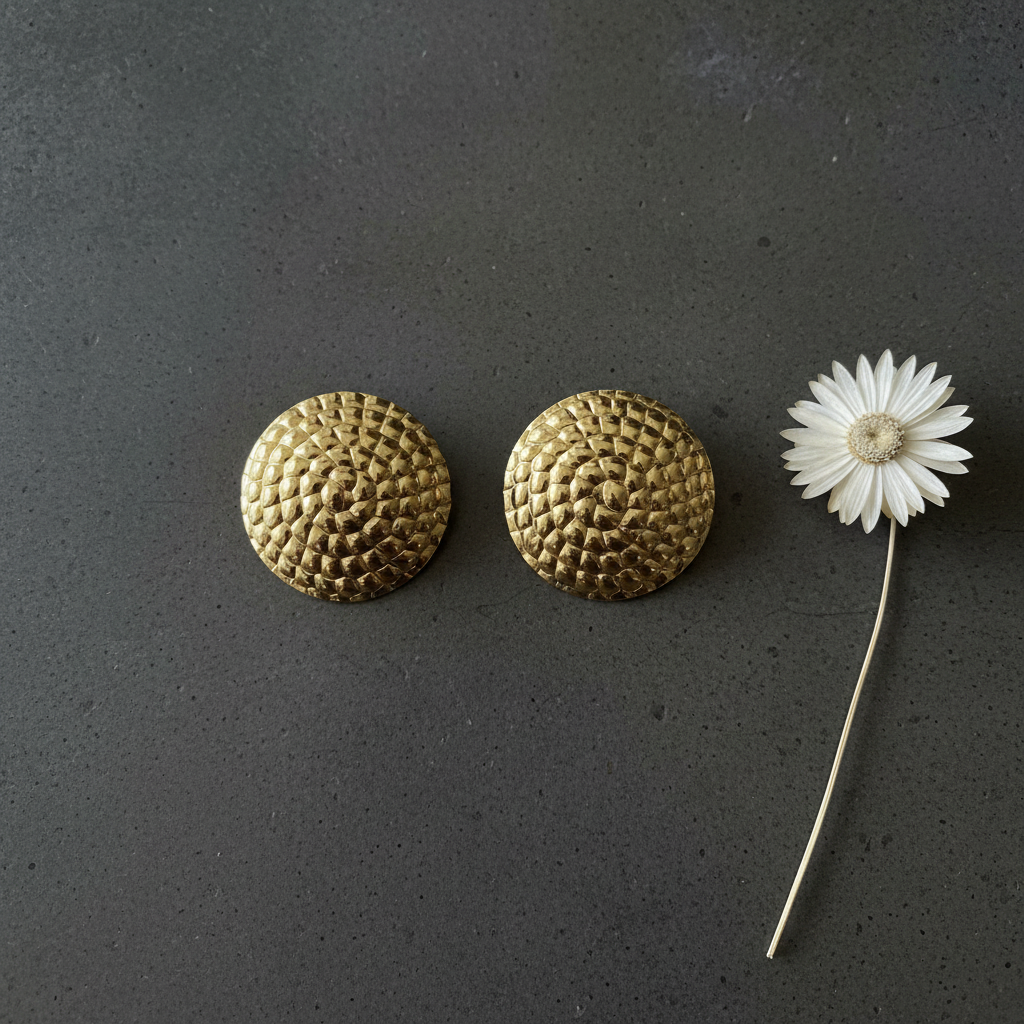 Gold scale dome earrings on concrete with flower